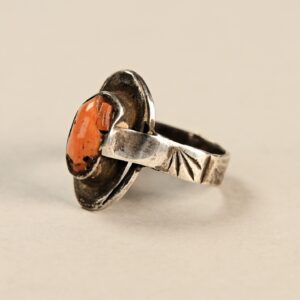 Piccolo anello antico in argento decorato con una perla di corallo al centro della parte frontale. Montatura con incisioni geometriche e motivi floreali, argento con patina antica.